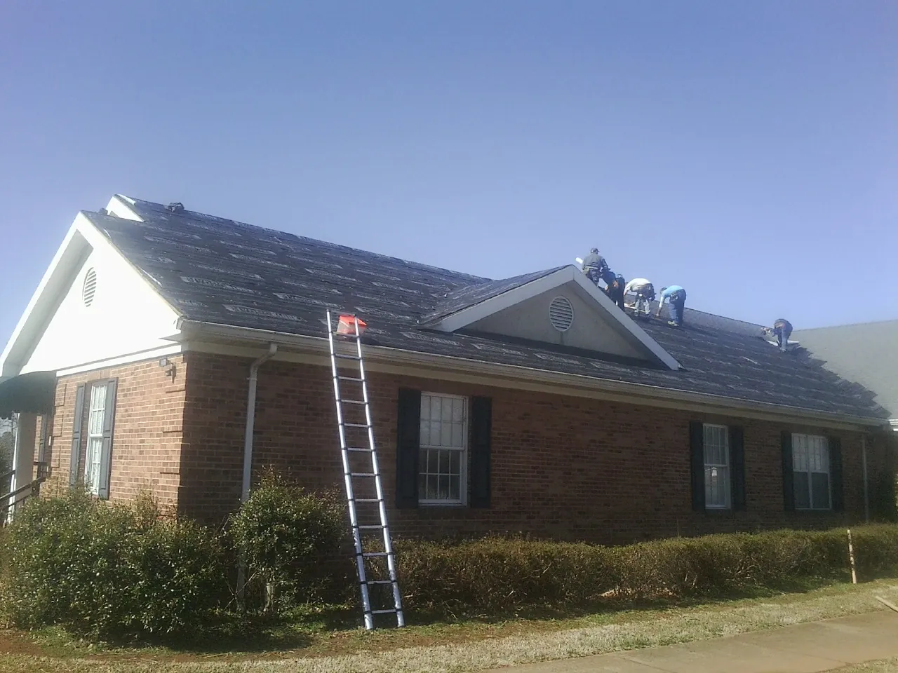 Crew tearing shingles off a brick ranch roof with a ladder set — Emergency Roof Repair work by our crew in Papillion