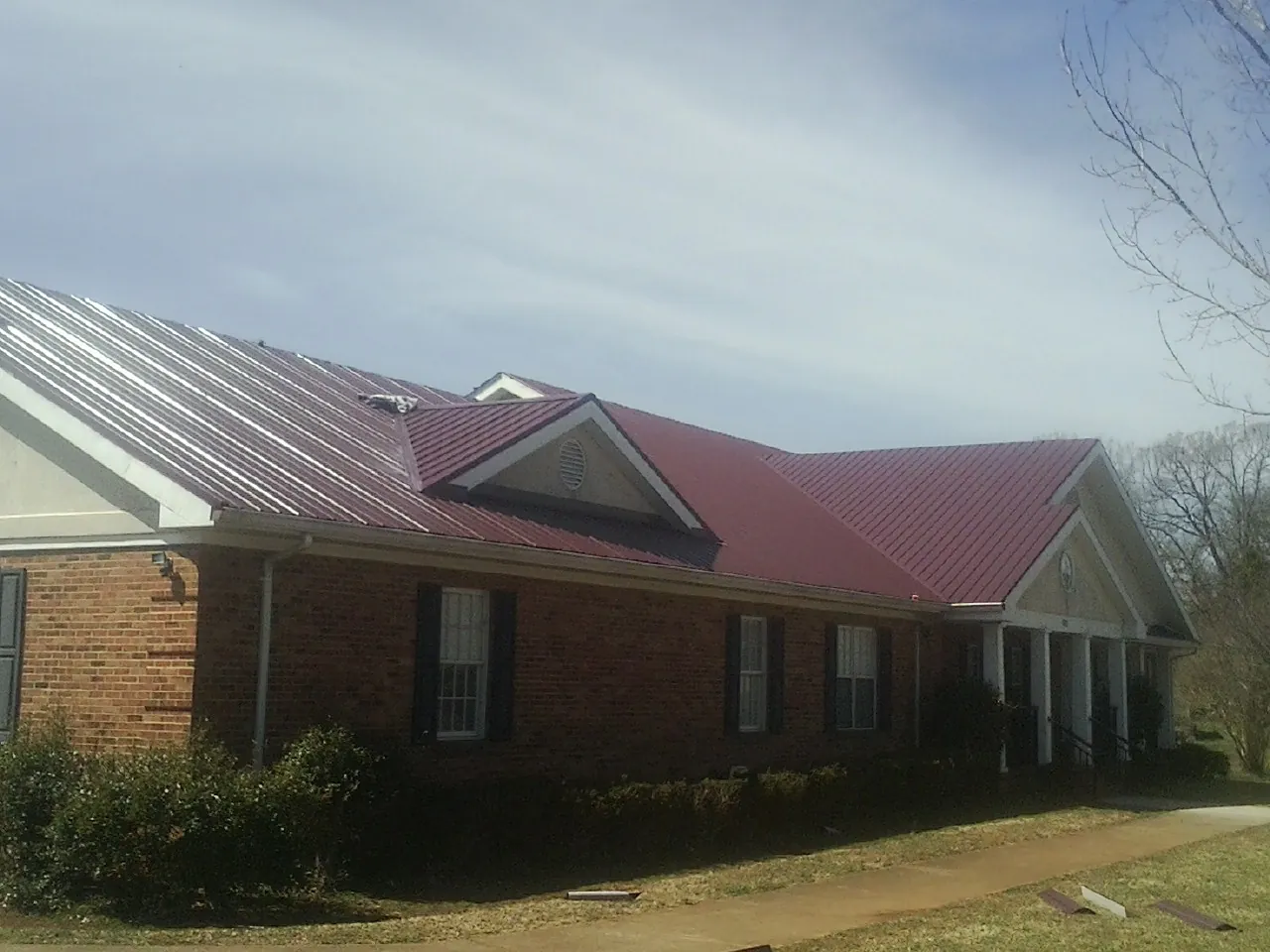 Red metal roof with gabled entries on a long brick building, from a Hail Damage Roof Repair job in Papillion