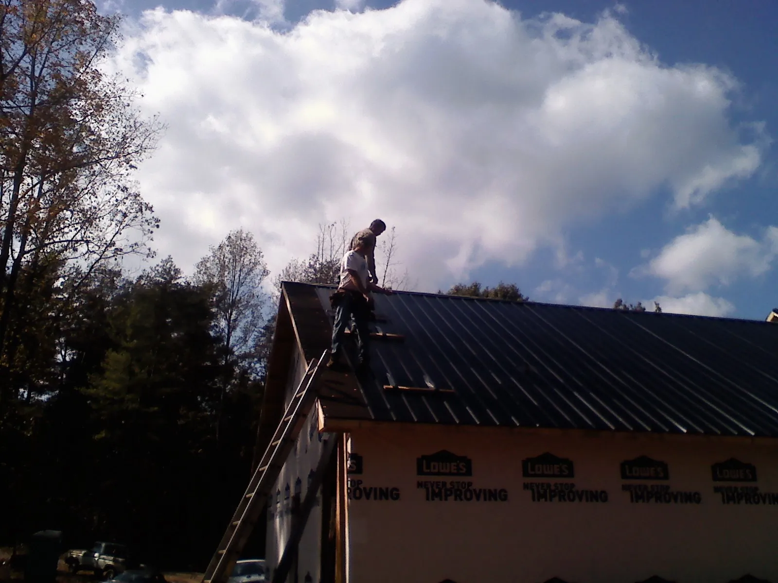 Roofer fastening dark metal panels high against a cloudy sky, from a Roof Inspection job in Papillion