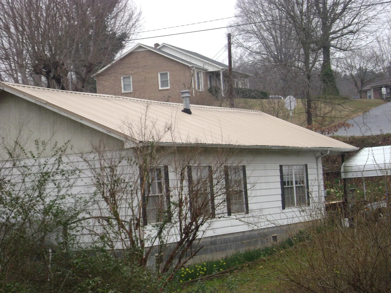 Tan metal roof on a white sided house set into a hillside — Commercial Roofing by Roofing Brothers in Papillion